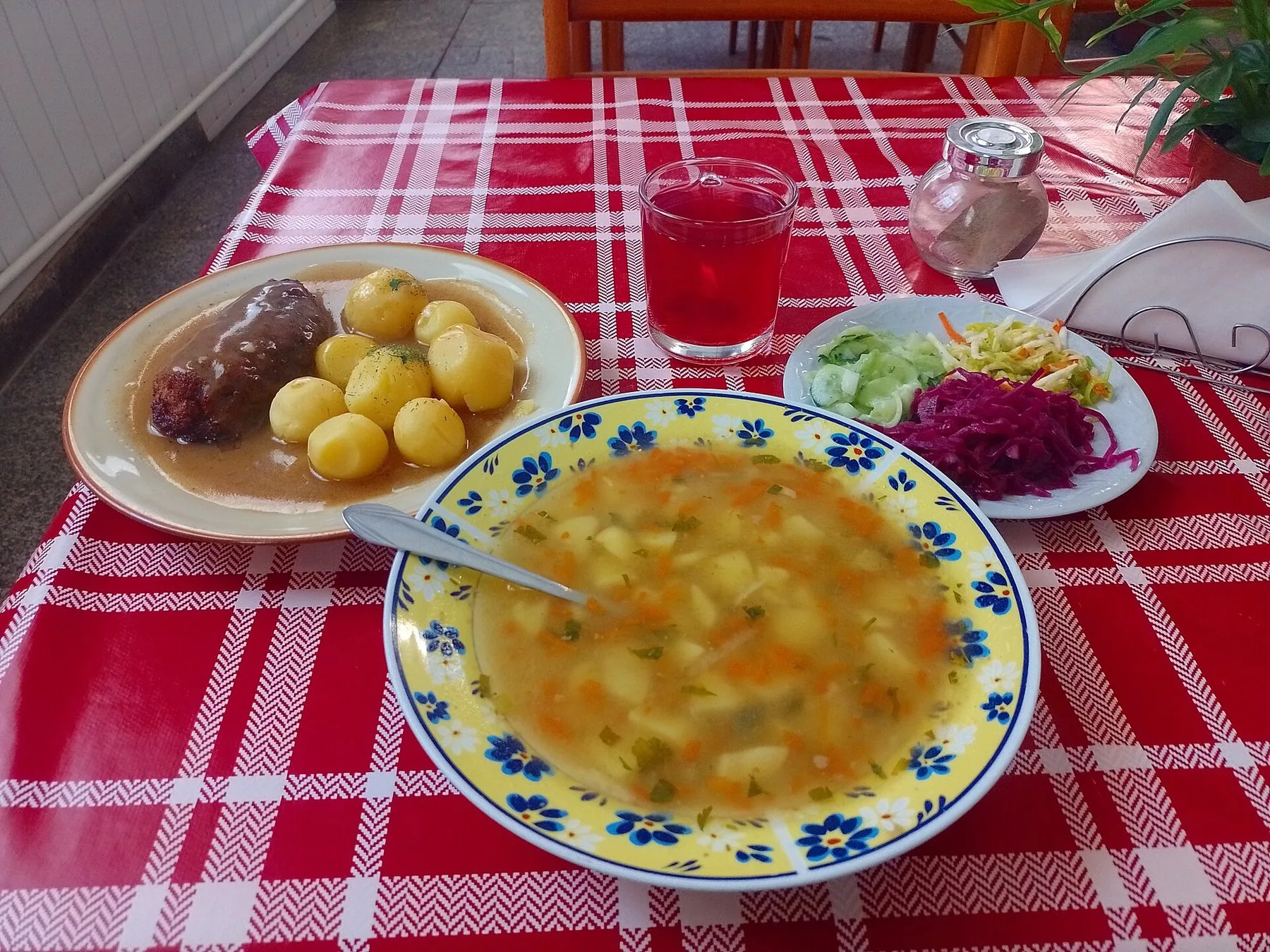 Frokost på en polsk mælkebar: grøntsagssuppe, kød med sovs, små kartofler, rødkålssalat og kompot på ternet dug