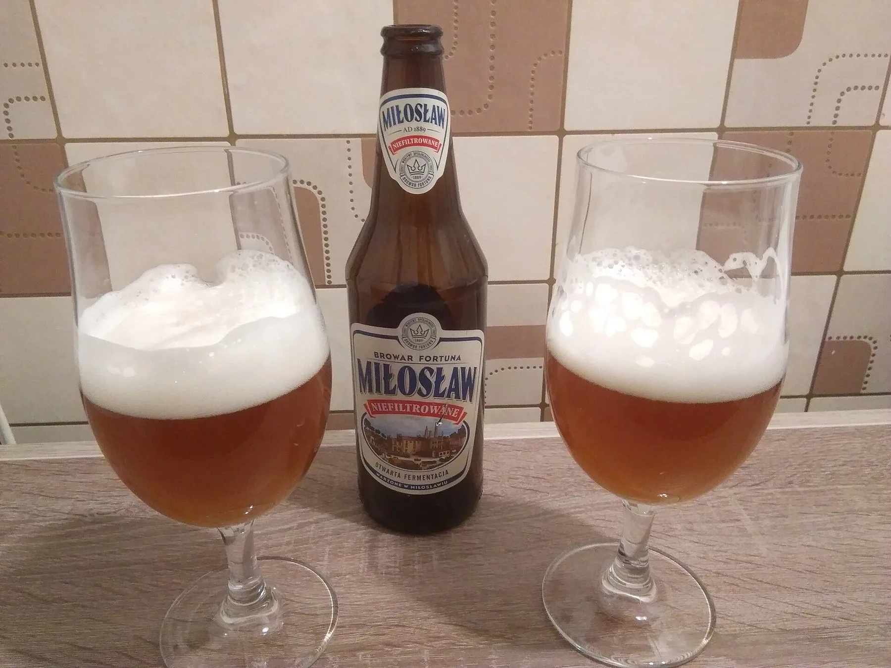 En flaska ofiltrerad polsk öl från bryggeriet Miłosław mellan två fyllda ölglas med skum