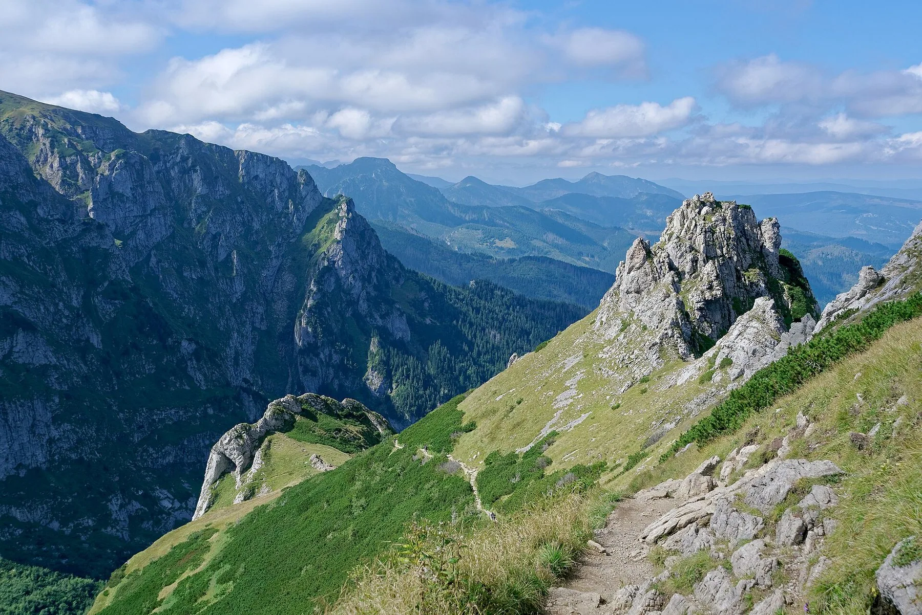 Rødmerket sti i gressbakker og kalksteinsklipper på sørsiden av Giewont i Tatra, med dype daler og fjell i bakgrunnen
