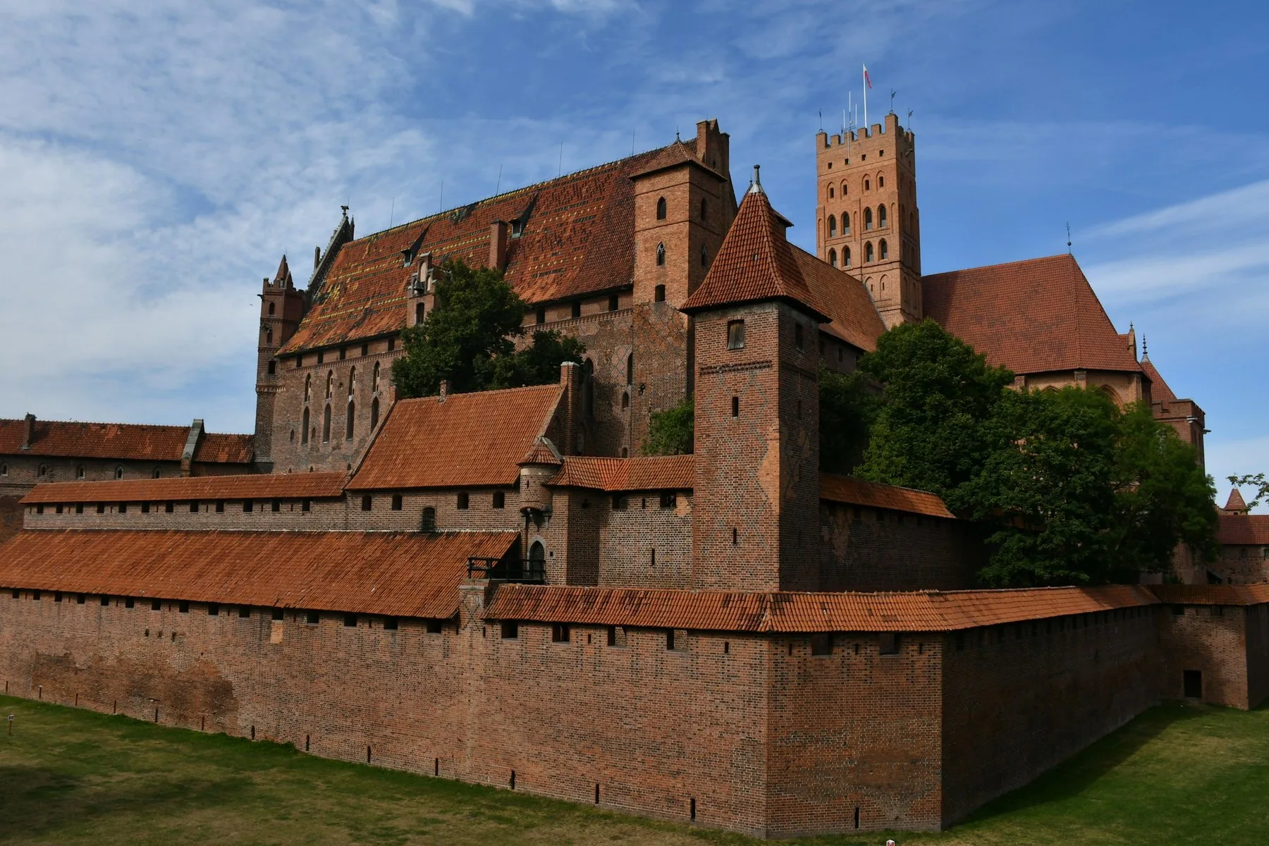 Ordensborgen i Malbork, verdens største teglstensborg, med ringmure og tårne under en blå himmel