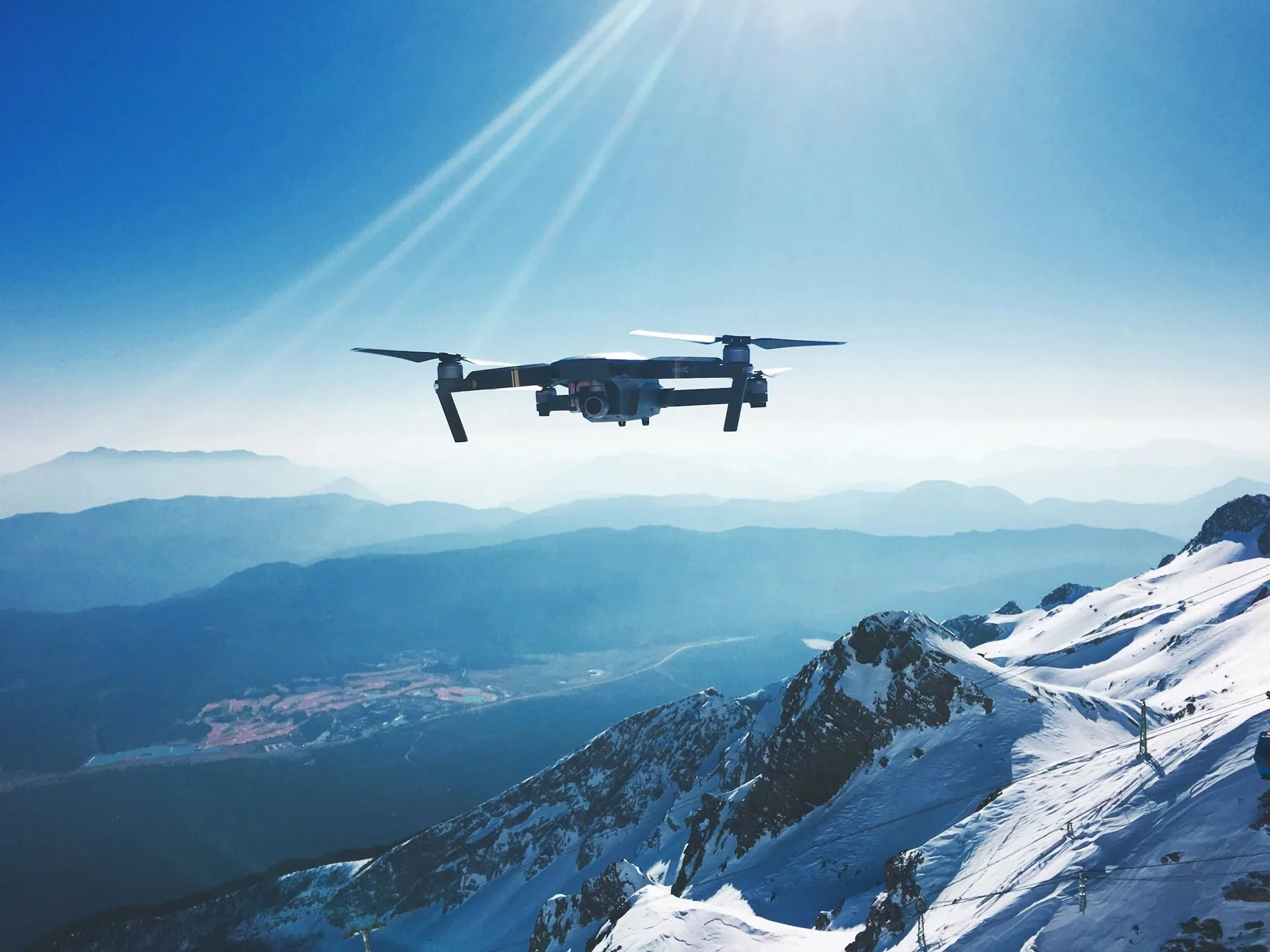 En hvit drone i luften foran snødekte fjell