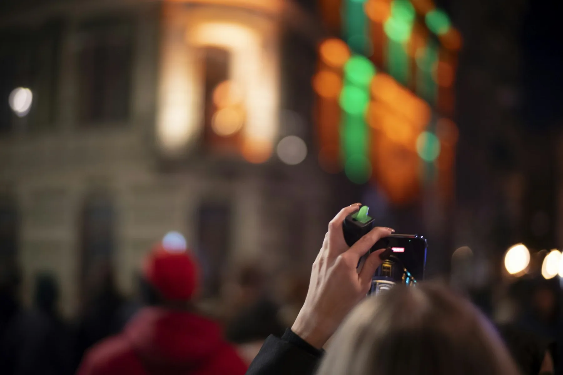 En hånd holder en mobiltelefon op og filmer en oplyst gade om aftenen
