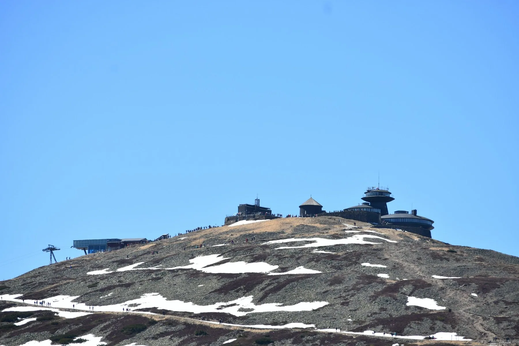Toppen av Śnieżka ovanför Karpacz med det runda observatoriet och snöfläckar på stenuren under blå himmel