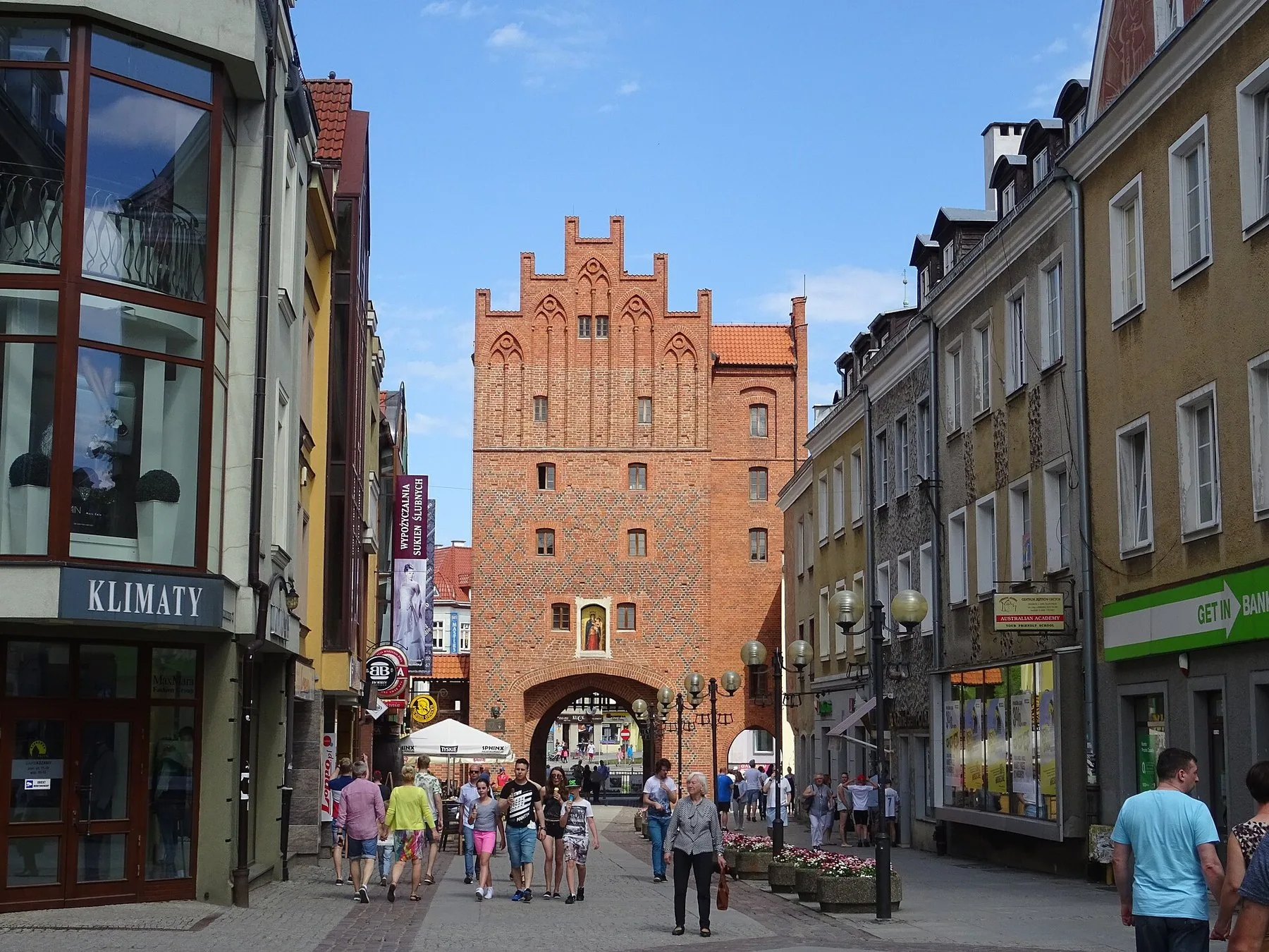 Den gotiska stadsporten Brama Wysoka i Olsztyn, sedd längs en gågata med färgglada hus