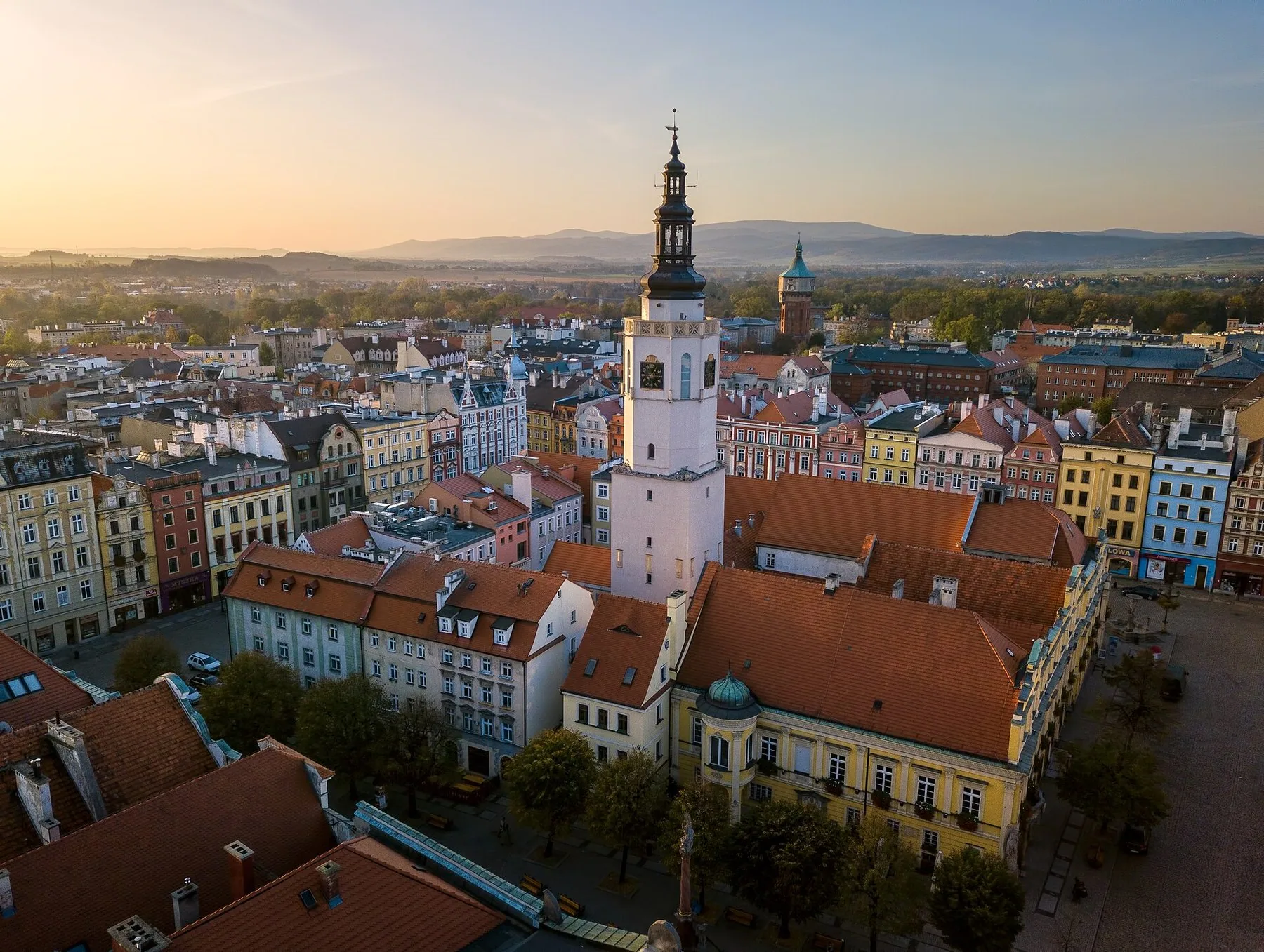 Rådhustårnet og de fargerike bygårdene rundt torget i Świdnica, sett fra lufta i kveldssol
