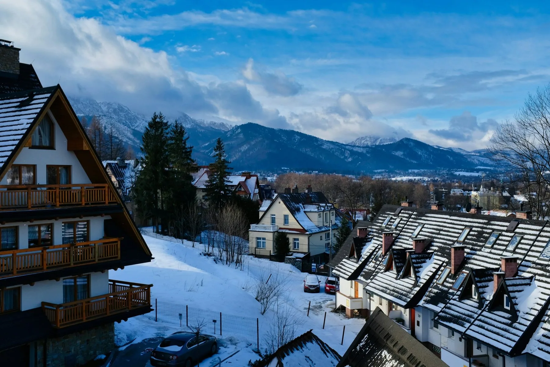 Snötäckta hustak och hus med balkonger i Zakopane, med Tatrabergen i bakgrunden