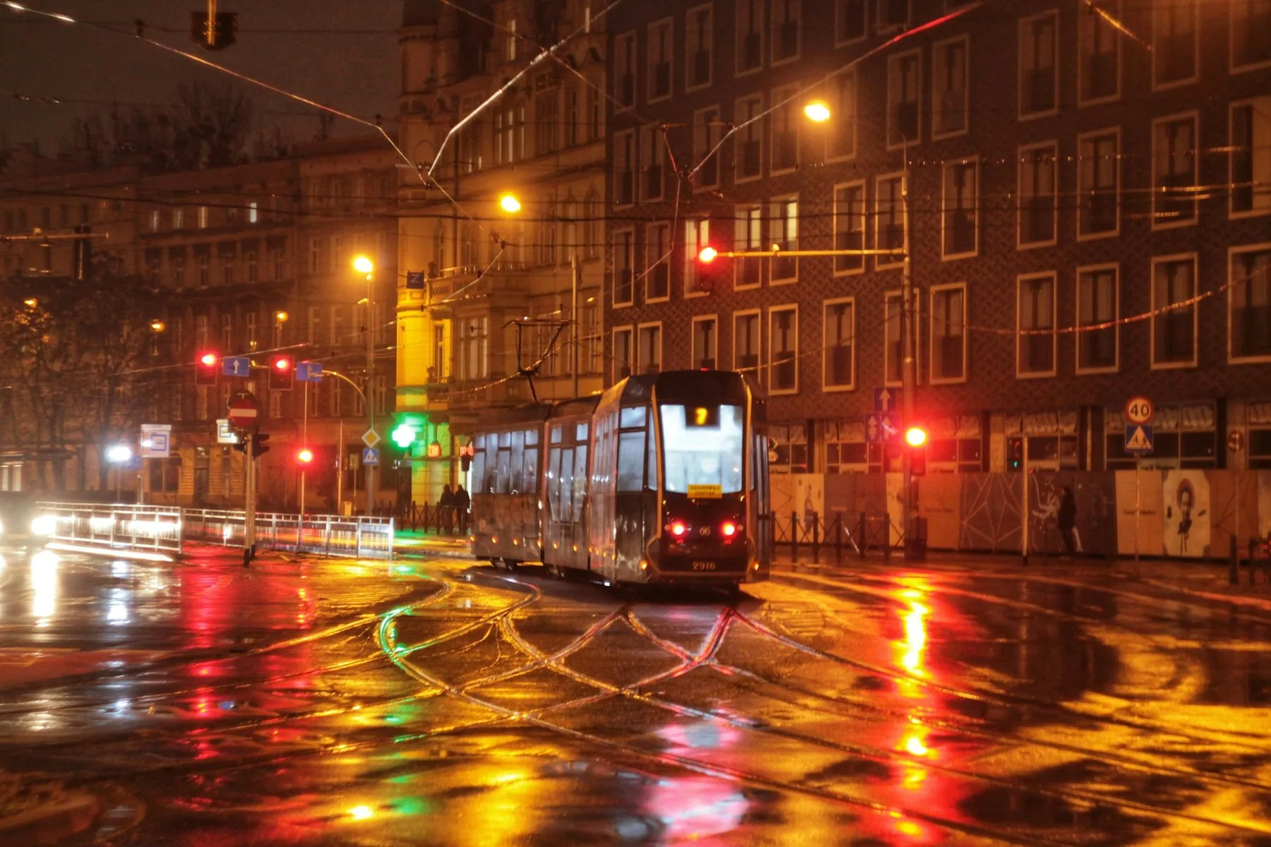 Sporvogn i bydelen Nadodrze i Wrocław en regnvåd aften med gadelys og trafiklys, der spejler sig i gaden